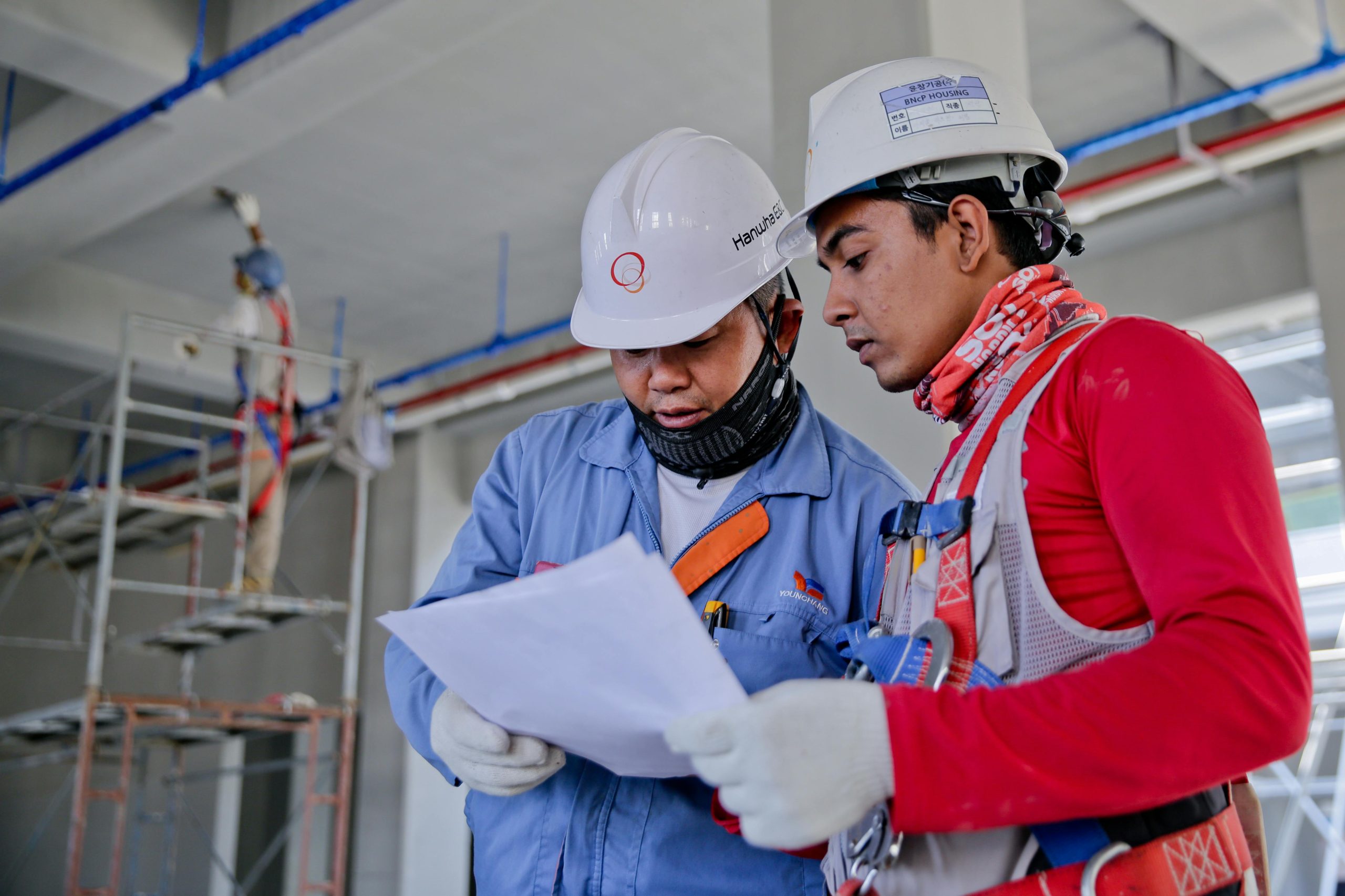 Servicios Two engineers in safety helmets reviewing construction plans at a worksite.